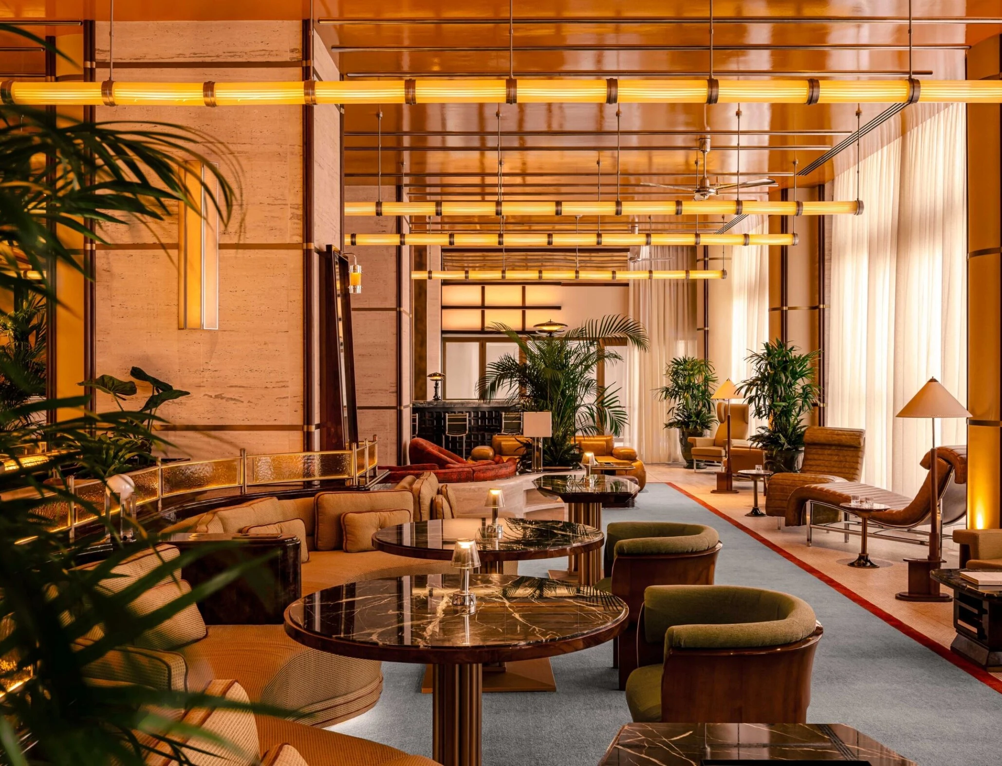 Salon Dolce Vita de l'Orient Express avec tables en marbre, banquettes courbes et éclairage chaud dans un décor planté